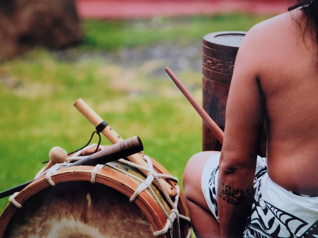 A person with cultural tattoos plays traditional drums outdoors, showcasing cultural heritage.